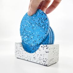 a hand touching a blue sponge on top of a white box with speckles