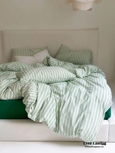 an unmade bed with green and white striped comforter on the bottom, next to a lamp