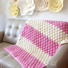 a pink and white crocheted blanket sitting on top of a couch next to flowers