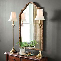 a mirror sitting on top of a wooden dresser next to a lamp and potted plant