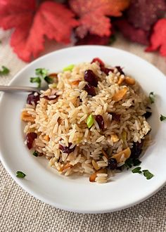 a white plate topped with rice and raisins on top of a table next to autumn leaves