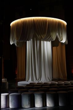 an empty stage with drapes and stools in the middle, lit by lights