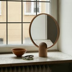 a mirror sitting on top of a window sill next to a bowl