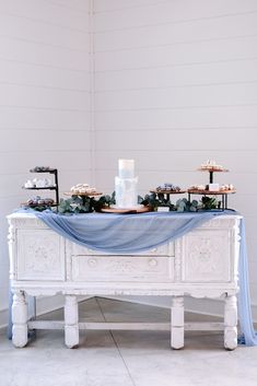 a table topped with lots of desserts on top of a white table covered in blue cloth