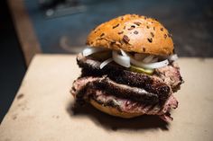 a large steak sandwich with onions and pickles on it sitting on a cutting board