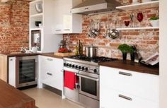 a kitchen with brick walls and white cabinets, stainless steel appliances and wooden counter tops