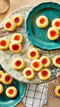 small cookies with jam on them sit on plates next to a cooling rack and glass of water