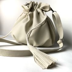 Bag made of extremely high quality synthetic material in off white. The lining is made with beige velvet, has an inner pocket with a zipper closure. All hardware is silver and the handle is 1.30 cm long, which can be adjusted to the desired size with the adjuster. Soft and lightweight bag with closure on the sides with drawstring and tassel at the ends made in the same material as the bag. The strap has carabiners which allow you to remove the strap. On the top it has a frilled detail that is given when closing and on the base pleats. It's great to take on trips as it can be put in your suitcase and doesn't get deformed (just open it and remove the strap to put it inside, it's important not to bend the rigid bottom).     Approximate measurements (Handmade product, slight variations may occ Cream Bucket Bag With Detachable Strap For Daily Use, Cream Bucket Bag With Detachable Strap, Beige Crossbody Bucket Bag With Removable Pouch, Trendy Cream Satchel Bucket Bag, Cream Hobo Bag With Zipper For Travel, Cream Crossbody Bucket Bag With Removable Pouch, Cream Hobo Bag For Travel With Zipper Closure, Beige Crossbody Bucket Bag With Detachable Handle, Beige Bucket Bag For Everyday Use