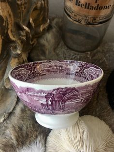 a purple and white bowl sitting on top of a table next to two balls of yarn