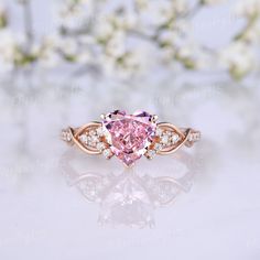 a pink heart shaped diamond ring with diamonds around the band and side stones on top