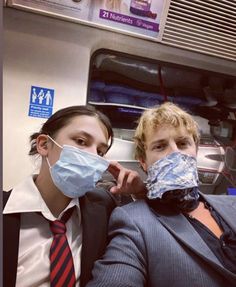 two people in suits and masks on a subway train, one wearing a face mask while the other wears a neck tie