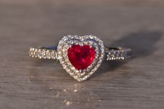 The 87th Avenue: Heart-Shaped Natural Ruby and Double Halo Natural Diamond Ring. This heartwarming ring features a captivating 0.75-carat vivid red natural ruby at its center, encircled by a double halo of round brilliant-cut natural diamonds. The diamonds gracefully continue down the shank, creating a seamless and luxurious design totaling 0.36 carats. Adding a modern touch, angular filigree details enhance the through-finger view. Crafted in 14-karat white gold, the ring is currently a finger Heart Shaped Ruby Engagement Ring, Heart-shaped Ruby Wedding Ring, Elegant Heart-shaped Ruby Ring For Proposal, Luxury Heart-shaped Ruby Engagement Ring, Heart-shaped Ruby Ring With Diamond For Gift, Heart-shaped Red Ruby Ring With Diamonds, Red Diamond Ring, Heart Halo Ring, Heart Shape Ring