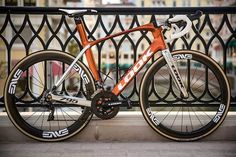 an orange bike parked on the side of a street next to a metal fence and railing