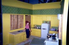 a doll is standing in a yellow kitchen