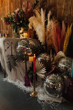 a table topped with lots of disco balls covered in mirrors and feathers next to candles