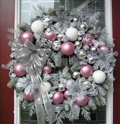 a christmas wreath on the front door with silver and pink ornaments hanging from it's side