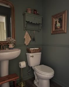 a white toilet sitting next to a sink in a bathroom under a mirror and a wooden shelf