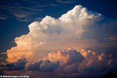 a large cloud is in the sky with some clouds behind it and a building on the other side