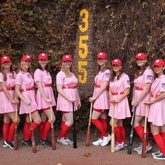 a group of women dressed in pink posing for a photo with baseball bats and uniforms