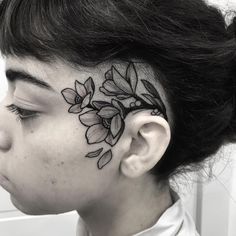 a woman with a flower tattoo on her face and behind her ear, looking to the side