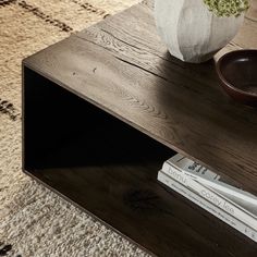 a wooden table topped with a white vase filled with flowers and two books on top of it