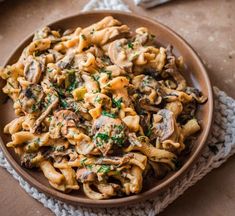 a bowl filled with pasta and mushrooms on top of a table next to a napkin