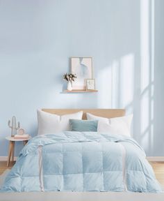 a bed with blue comforter and pillows in a light blue room next to a window