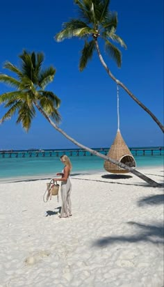 a woman standing on top of a sandy beach next to palm trees and the ocean