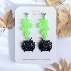 the black and green earrings are on display next to some leafy leaves with white speckles