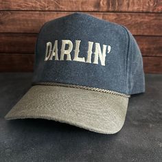 Vintage Style Darlin' Embroidered Faded Canvas Snapback Trucker Rope Hat with Free Shipping. White stitched text/logo. Condition is "New with tags". Shipped with USPS First Class. Step into the world of the great outdoors with our Darlin' Stitched Faded Canvas Rope Hat. With its faded canvas and rope accents, this hat exudes rustic charm and pays tribute to the iconic country music legends. Plus, enjoy free shipping on this vintage-inspired accessory that's perfect for any country music enthusia Vintage Outdoor Baseball Cap With Embroidered Logo, Adjustable Cotton Trucker Hat With Letter Embroidery, Vintage Snapback Hat With Letter Print For Outdoor, Vintage Letter Print Snapback Hat For Outdoor, Vintage Outdoor Hat With Letter Print, Vintage Letter Print Hat For Outdoor, Vintage Letter Print Outdoor Hat, Trucker Hat With Letter Print In Cotton, Vintage Cotton Snapback Hat With Embroidered Logo