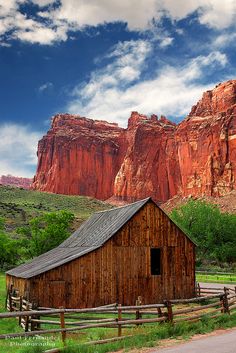 an old barn sits in front of the red rock formations on a sunny day with a blue sky and white clouds