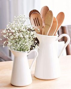 two white pitchers filled with wooden spoons and baby's breath on top of a table