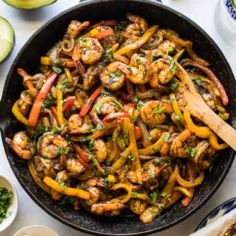 a skillet filled with shrimp and peppers next to sliced avocado on a table