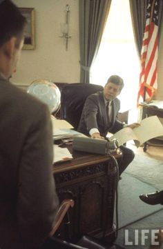 a man sitting at a desk with papers in front of him and an american flag behind him