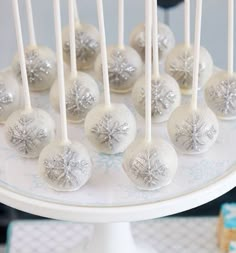 white cake pops with silver snowflakes on them sitting on top of a plate