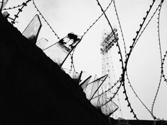 barbed wire surrounds the top of an old building with a tower in the back ground