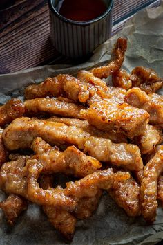 chicken wings are piled on top of wax paper next to a cup of dipping sauce