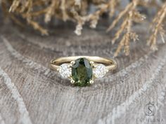 a green and white diamond ring sitting on top of a wooden table next to some branches