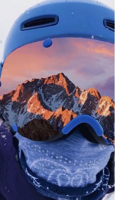 a snowboarder wearing a helmet and goggles with mountains reflected in the lens