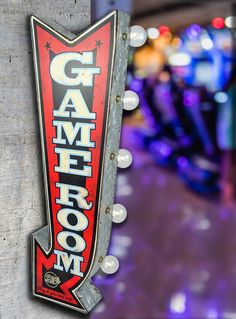 a sign that says game room hanging on the side of a building with lights in the background