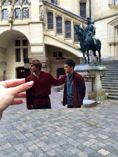 two people standing in front of a building with a horse statue on the corner and one person holding up a small toy