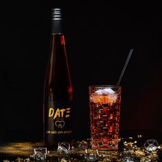 a bottle and glass filled with liquid next to ice cubes on a black surface