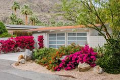 a house with pink flowers in front of it and mountains behind the house, on a sunny day