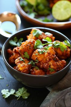 two bowls filled with food and garnished with cilantro, parsley and lime