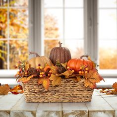 a wicker basket filled with pumpkins and other autumn leaves on a table in front of a window