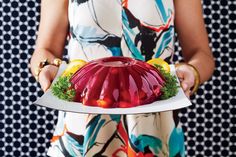 a woman is holding a plate with a jelly cake on it and garnished with lemons