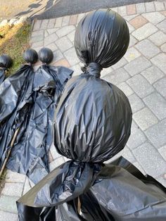 two black trash bags sitting on top of a sidewalk next to each other with one bag wrapped around it's head