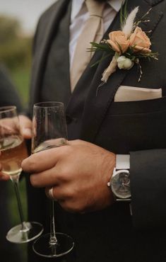 a man in a tuxedo holding two wine glasses with flowers on the side