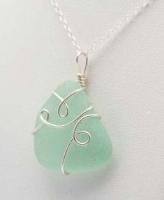 a green sea glass necklace with silver wire on a white background, hanging from a sterling plated chain