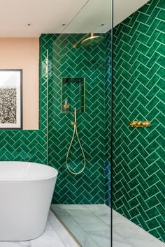 a green tiled bathroom with a white bathtub and gold fixtures on the wall, along with a shower head